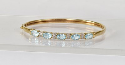 Lot 859 - A 9ct yellow gold bangle set with blue and...