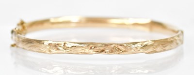 Lot 1413 - A 9ct yellow gold hinged bangle with foliate...
