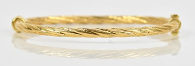 Lot 27 - A textured yellow metal hinged snap bangle,...