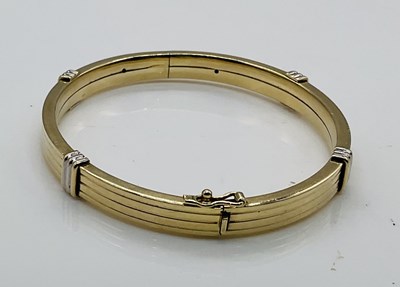 Lot 565 - A 9ct yellow gold bangle, with white gold...