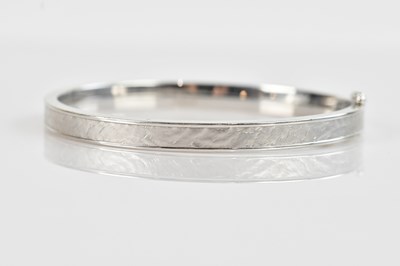Lot 1177 - A white textured metal hinged snap bangle,...