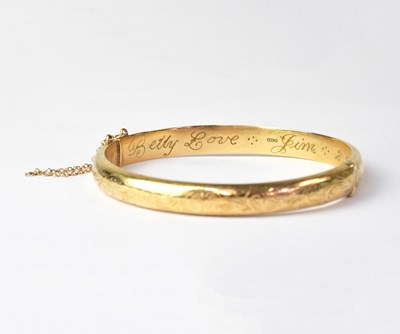 Lot 1019 - A 9ct yellow gold hinged bangle with engraved...