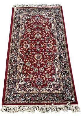 Lot 128 - A red ground floral decorated rug with blue...