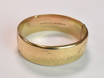 Lot 408 - A 9ct yellow gold oval engraved hinged bangle,...