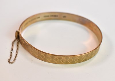 Lot 427 - A 9ct yellow gold engraved oval hinged bangle,...