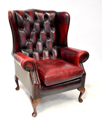 Lot 10 - A modern oxblood red leather button wing back armchair